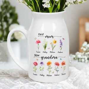 Pu&ograve; includere: Brocca in ceramica bianca con manico, piena di fiori bianchi. La brocca &egrave; decorata con illustrazioni floreali e la scritta "First mom, now grandma" con nomi sotto i fiori.