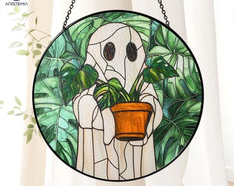 May include: A stained glass window hanging with a white ghost holding a potted plant with green leaves. The background is a green leafy pattern.