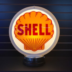 May include: A white, round, illuminated sign with a red and yellow shell logo and the word "SHELL" in red letters.