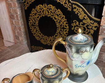 May include: A vintage tea set with a teapot, sugar bowl, and creamer. The set features a black and gold design with gold accents. The teapot has a curved spout and handle. The sugar bowl has a lid. The creamer has a small handle.
