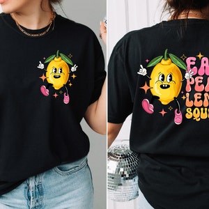 Może przedstawiać: Czarny T-shirt z postacią kreskówkowego cytryny z przodu i napisem "Easy Peasy Lemon Squeezy" z tyłu.