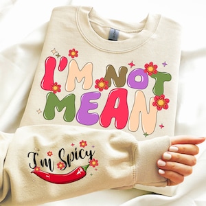 May include: A beige sweatshirt with the text "I'm not mean I'm spicy" in colorful letters and a red chili pepper graphic. The text is surrounded by small flowers.