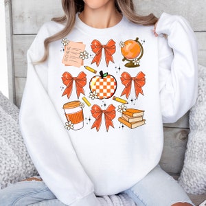 May include: White sweatshirt with an orange and white checkered apple, orange bows, pencils, a coffee cup, books, and a globe. The text on the checklist says "To Do List".