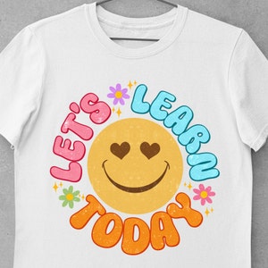 May include: White t-shirt with a colorful graphic design featuring a smiley face with hearts for eyes and the text "Let's Learn Today".