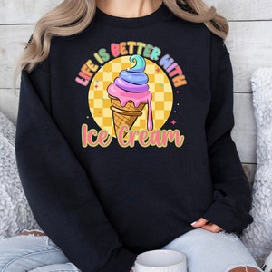 Puede incluir: Sudadera negra con un gr&aacute;fico de un cono de helado colorido y el texto "Life is better with ice cream".