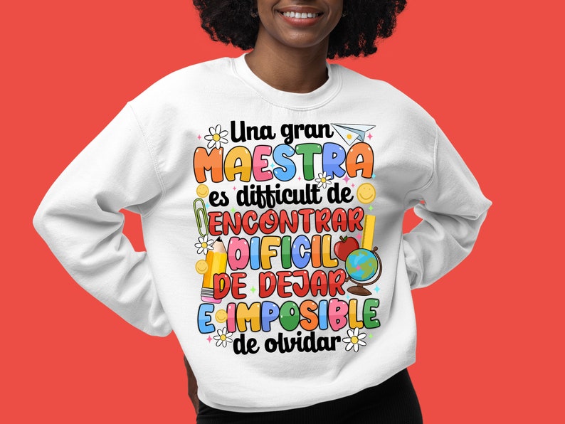 Op de afbeelding: Wit sweatshirt met een kleurrijk grafisch ontwerp met de tekst "Una gran maestra es difficult de encontrar, dificil de dejar, e imposible de olvidar". De grafiek bevat illustraties van een potlood, een aardbol, een boek en een bloem.