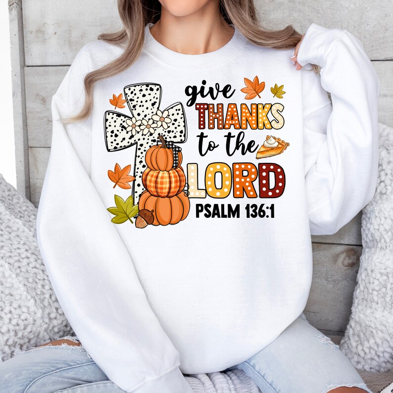 May include: White sweatshirt with a graphic of a cross, pumpkins, and a pie. The text reads "give thanks to the Lord Psalm 136:1".