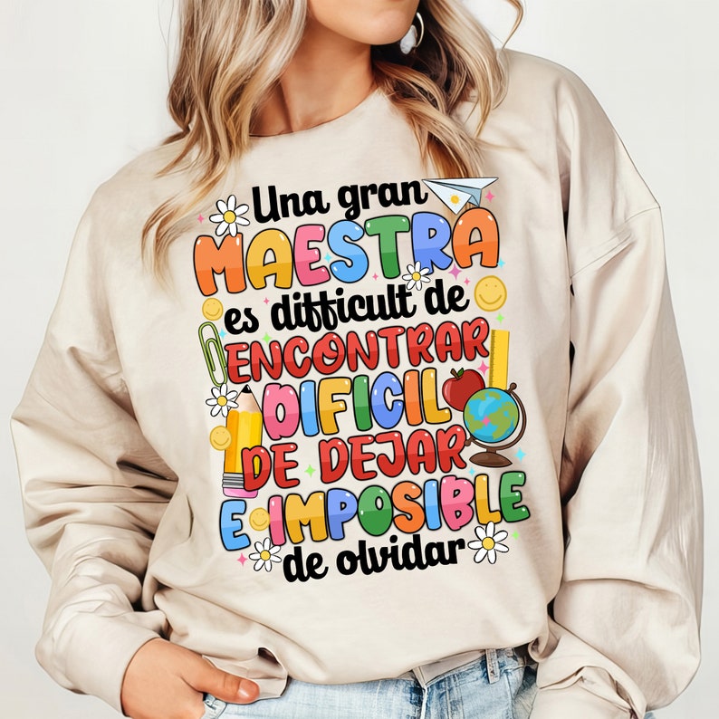 Op de afbeelding: Een beige sweatshirt met een kleurrijk grafisch ontwerp met de tekst "Una gran MAESTRA es difficult de ENCONTRAR DIFCIL DE DEJAR E IMPOSIBLE de olvidar".