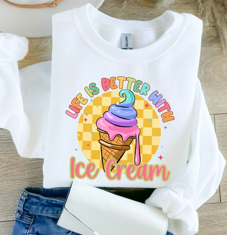 Puede incluir: Sudadera blanca con un gr&aacute;fico de cono de helado colorido y el texto "Life is better with ice cream".