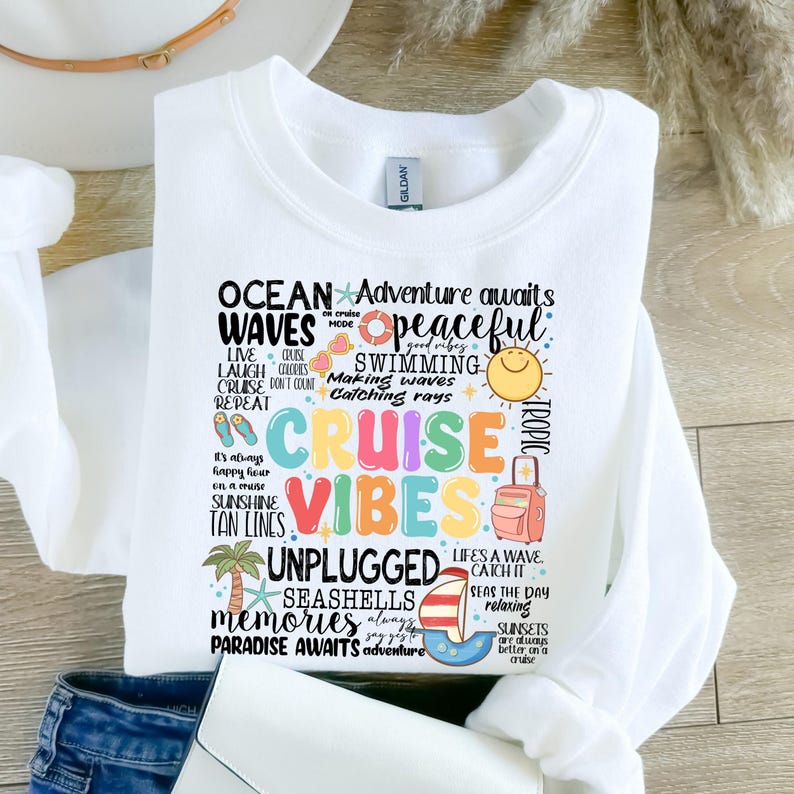 Peut inclure: Sweat-shirt blanc avec un motif graphique color&eacute; comportant les mots "Ocean Waves", "Cruise Vibes", "Unplugged", "Seashells", "Memories", et "Paradise Awaits". Le graphique comprend &eacute;galement des images d'un bateau de croisi&egrave;re, d'une valise, d'un palmier et d'un coquillage.