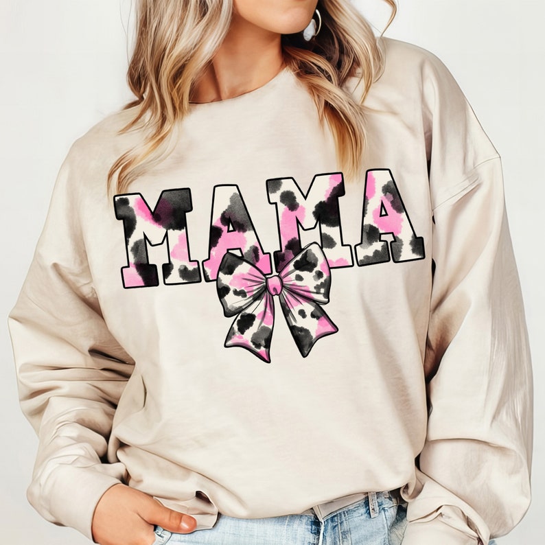 May include: A beige sweatshirt with the word "MAMA" printed in black with a pink and black leopard print design. A pink and black leopard print bow is below the word.
