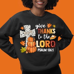 May include: Black sweatshirt with a white and black cross, pumpkins, and fall leaves. The text reads "give THANKS to the LORD PSALM 136:1".