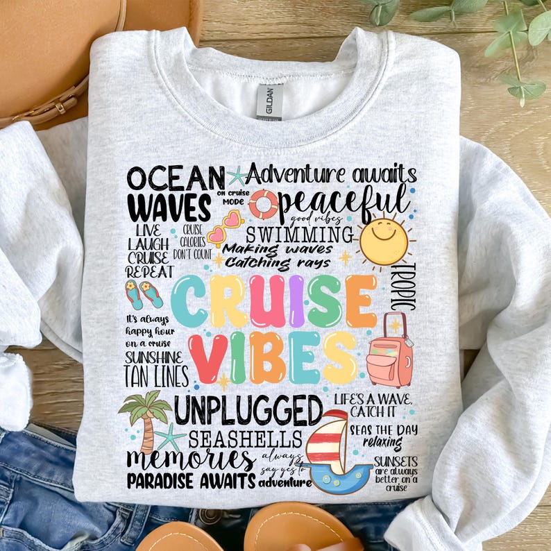 Peut inclure: Un sweat-shirt gris avec un imprim&eacute; graphique color&eacute; qui dit "Ocean Waves Cruise Vibes" et comprend des phrases comme "Adventure awaits", "Peaceful", "Swimming", "Making waves", "Catching rays", "Unplugged", "Seashells", "Memories", "Paradise awaits", et "Life's a wave, catch it".