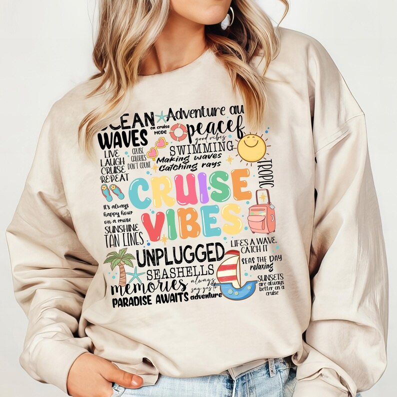 Peut inclure: Un sweat-shirt beige avec un imprim&eacute; graphique color&eacute; qui dit "Ocean Waves Cruise Vibes Unplugged Seashells Memories Paradise Awaits Adventure". Le graphique comprend &eacute;galement une vari&eacute;t&eacute; d'images nautiques et tropicales, comme un soleil, un palmier, une valise et un bateau.