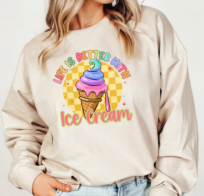 Puede incluir: Una sudadera beige con el texto "Life is better with ice cream" impreso en la parte delantera. El texto est&aacute; en colores arco&iacute;ris y hay un cono de helado de dibujos animados con chispas de arco&iacute;ris y un fondo amarillo.