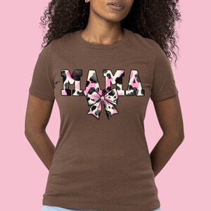 May include: A brown t-shirt with the word "MAMA" printed in pink and black animal print. A pink and black animal print bow is below the word.