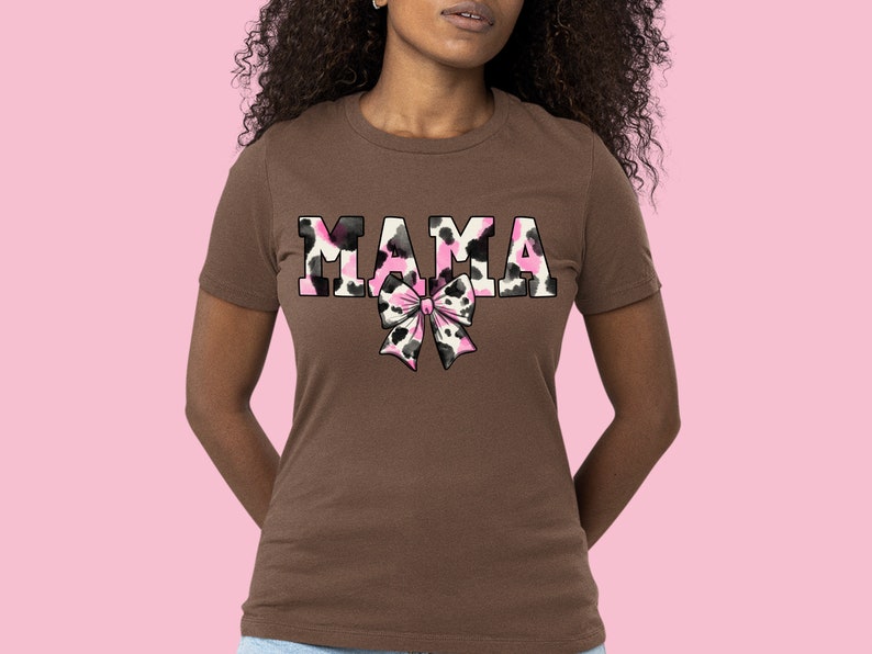 May include: A brown t-shirt with the word "MAMA" printed in pink and black animal print. A pink and black animal print bow is below the word.