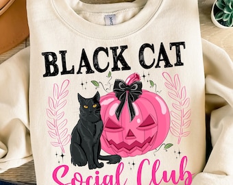 May include: Cream-colored sweatshirt featuring a black cat, a pink jack-o'-lantern with a black bow, and the text "BLACK CAT Social Club" in black and pink. The design includes decorative leaf accents, perfect for Halloween.