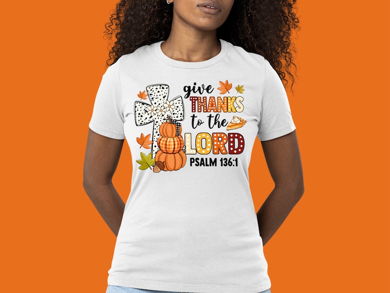 May include: White t-shirt with a graphic of a cross, pumpkins, and fall leaves. The text reads "give THANKS to the LORD PSALM 136:1".
