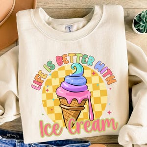 Puede incluir: Una sudadera de color crema con un gr&aacute;fico colorido de un cono de helado y el texto "Life is better with ice cream".