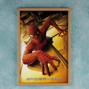 May include: A poster featuring a red and blue Spiderman character crawling on a yellow and gold surface. The text "SPIDER-MAN" is printed in silver at the bottom of the poster.