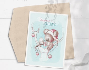 May include: A Christmas card featuring a koala wearing a Santa hat and holding a gift, with a bird perched on a branch beside it. The card has a blue background with white branches and red ornaments. The text "Seasons Greetings" is written in pink at the top of the card.
