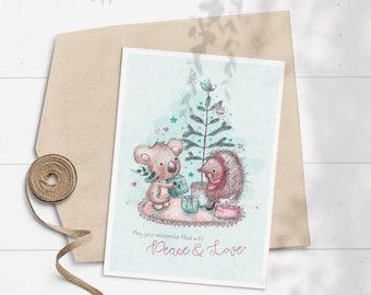 May include: A Christmas card featuring a koala and a hedgehog standing by a decorated Christmas tree. The card has a light blue background with pink hearts and stars. The text on the card reads "May your season be filled with Peace & Love."
