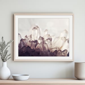 Pu&ograve; includere: Una stampa artistica da parete orizzontale incorniciata che raffigura un gruppo di cristalli di quarzo traslucidi e appuntiti in tonalit&agrave; di bianco, grigio e viola intenso. L'opera &egrave; esposta in una cornice di legno chiaro sopra una console.