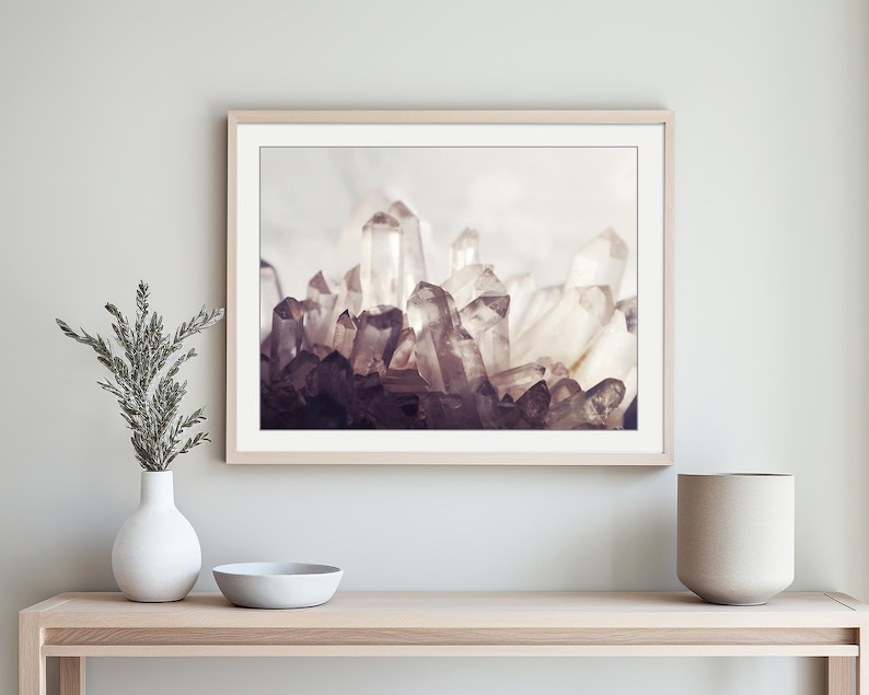 Pu&ograve; includere: Una stampa artistica da parete orizzontale incorniciata che raffigura un gruppo di cristalli di quarzo traslucidi e appuntiti in tonalit&agrave; di bianco, grigio e viola intenso. L'opera &egrave; esposta in una cornice di legno chiaro sopra una console.