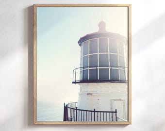 May include: A framed wall art print featuring a white lighthouse with a dark metal railing and a grid-patterned lantern room. The structure is set against a pale, hazy sky and ocean background, captured in a light, airy color palette.