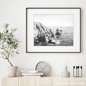 May include: A black and white landscape photograph of a rocky coastline with ocean waves, displayed in a thin black frame. The text Lupen Grainne Photography is printed in white in the bottom right corner of the image.