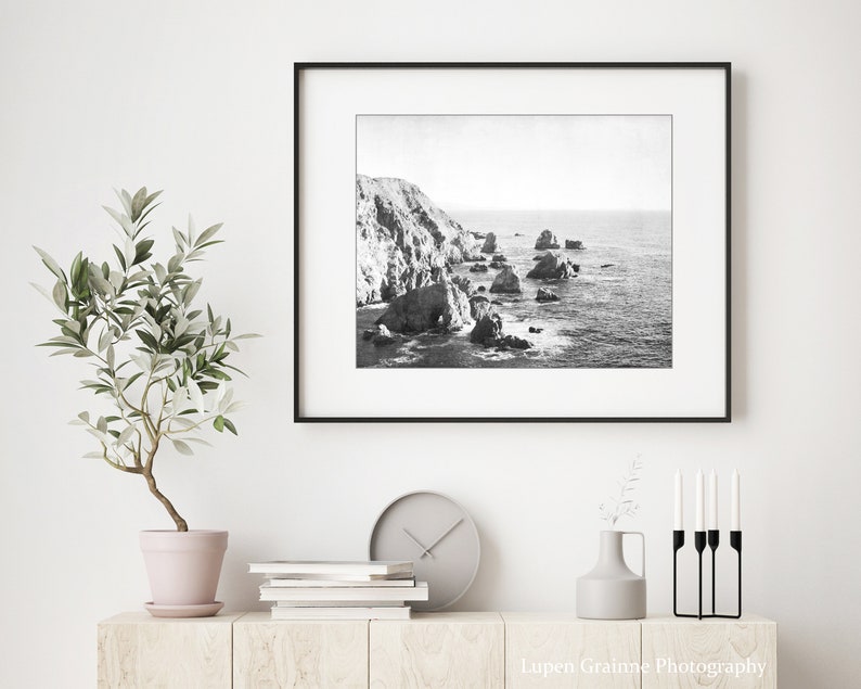 May include: A black and white landscape photograph of a rocky coastline with ocean waves, displayed in a thin black frame. The text Lupen Grainne Photography is printed in white in the bottom right corner of the image.