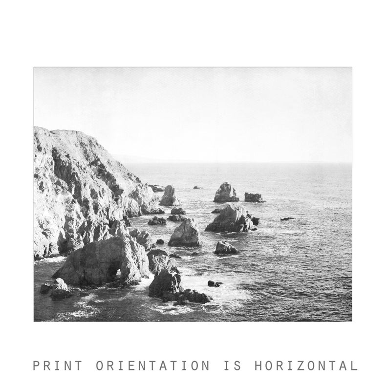 May include: A black and white landscape photograph featuring a rugged rocky coastline meeting the ocean. Jagged cliffs and scattered rock formations rise from the water under a bright sky. The text PRINT ORIENTATION IS HORIZONTAL appears below.
