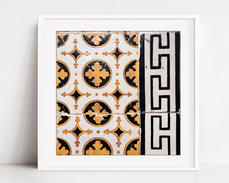 May include: A framed print of a close-up of a vintage tile pattern. The tile is white with black and gold geometric designs. The tile is cracked in the center.
