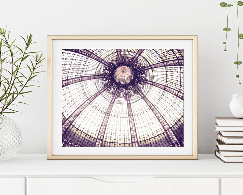 May include: A framed print featuring a detailed architectural image of a glass dome. The image showcases a symmetrical design with intricate patterns and a central focal point, all in shades of purple and white. The print is set in a gold frame.