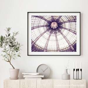 May include: A framed print of a detailed architectural ceiling with a circular design in shades of purple and white. The print is displayed above a wooden cabinet with a potted plant, books, a clock, and decorative items.