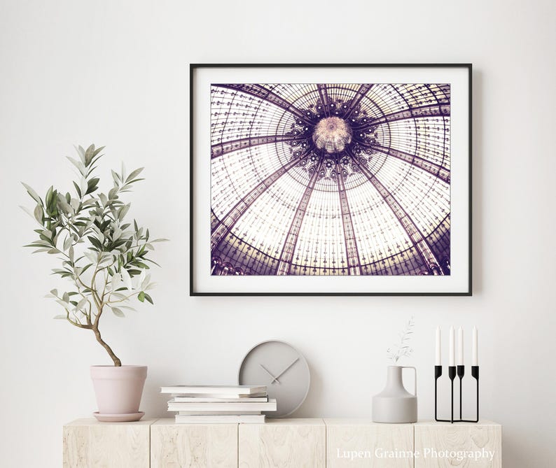 May include: A framed print of a detailed architectural ceiling with a circular design in shades of purple and white. The print is displayed above a wooden cabinet with a potted plant, books, a clock, and decorative items.