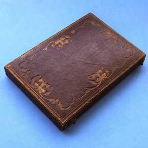 Pode incluir: Um álbum de fotos de couro marrom com um design floral em relevo dourado.