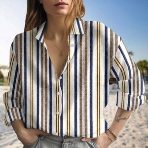May include: A button-down shirt with vertical stripes in white, brown, navy blue, and yellow. The long-sleeved shirt has a collared neckline and is unbuttoned at the top. The background shows a beach scene.