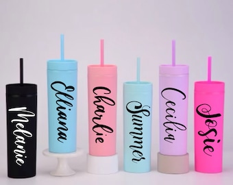 May include: Five personalized tumblers with straws. The tumblers are in various colors: black, light blue, pink, light blue, and pink. Each tumbler has a name written on it: Melanie,  Eliana, Charlie, Summer, and Josie.