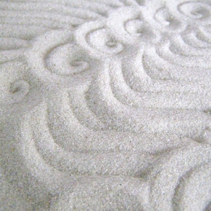 May include: A close-up of a white sand surface with a decorative pattern created by lines and swirls.