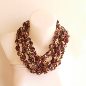 Może przedstawiać: Wielowarstwowy naszyjnik wykonany na szydełku z brązowej, czerwonej, żółtej i białej przędzy. Naszyjnik składa się z małych, szydełkowych kulek.