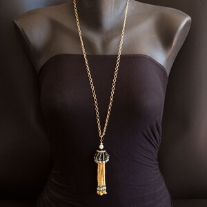 May include: A gold chain necklace with a black and blue beaded tassel pendant. The necklace is displayed on a black mannequin.