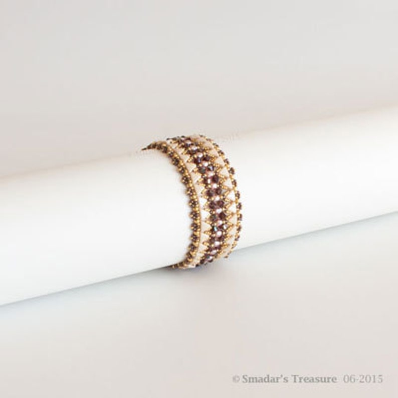 May include: A white and brown beaded bracelet with a geometric pattern. The bracelet is made with small, round beads and is wrapped around a white surface.