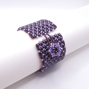 Op de afbeelding: Een paarse en bruine kralen armband met een bloemvormig ontwerp in het midden.