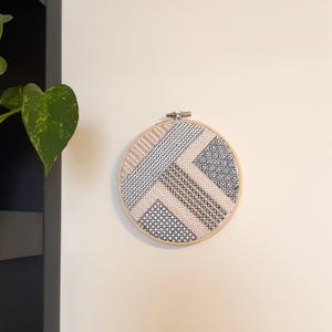 幾何学模様の刺繍入りテキスタイルアート、壁掛けまたは棚ディスプレイ、黒、白、ベージュ。丸いフレームのテクスチャ刺繍