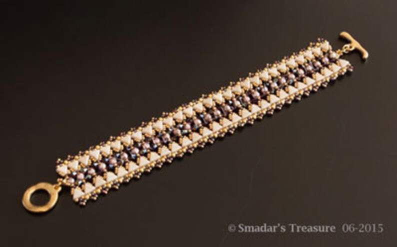May include: A gold and white beaded bracelet with a geometric pattern. The bracelet is made with small, round beads and has a toggle clasp.