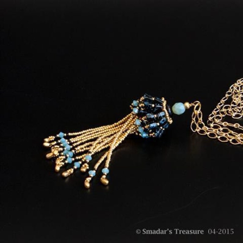May include: A gold chain necklace with a blue and black beaded tassel pendant. The tassel is made of small, round beads and has a fringe at the bottom.