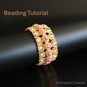 May include: A beaded bracelet with a floral design. The bracelet features gold-colored beads, with pink and white pearl accents. The words "Beading Tutorial" are in the upper left corner. The bracelet is displayed on a black surface.