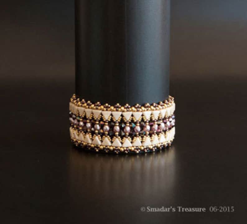 May include: A beaded bracelet with a geometric pattern in shades of brown, white, and pink. The bracelet is made with small, round beads and has a delicate, feminine look.